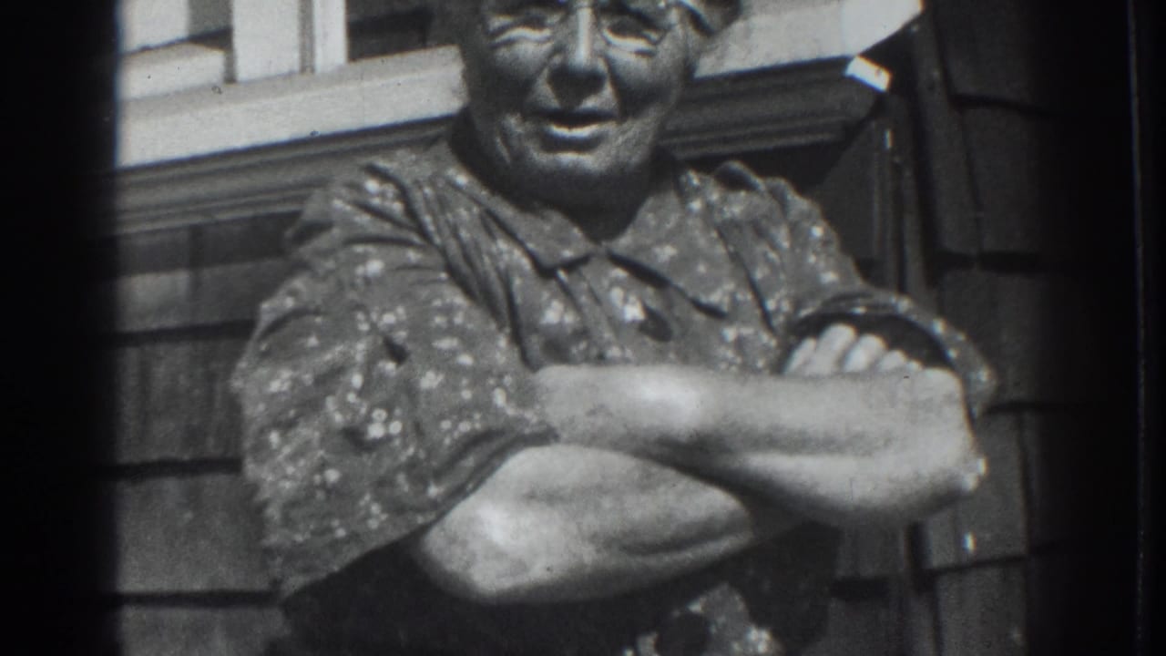 Older woman with folded arms smiling outside a house.
