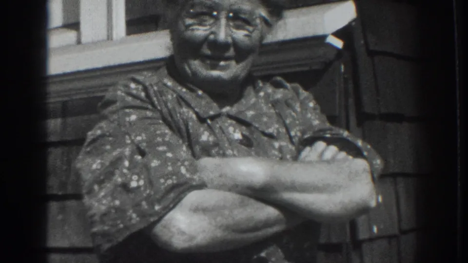 Chest-up view of an older woman smiling in a patterned dress, filmed outside a Vacaville residence in 1937.