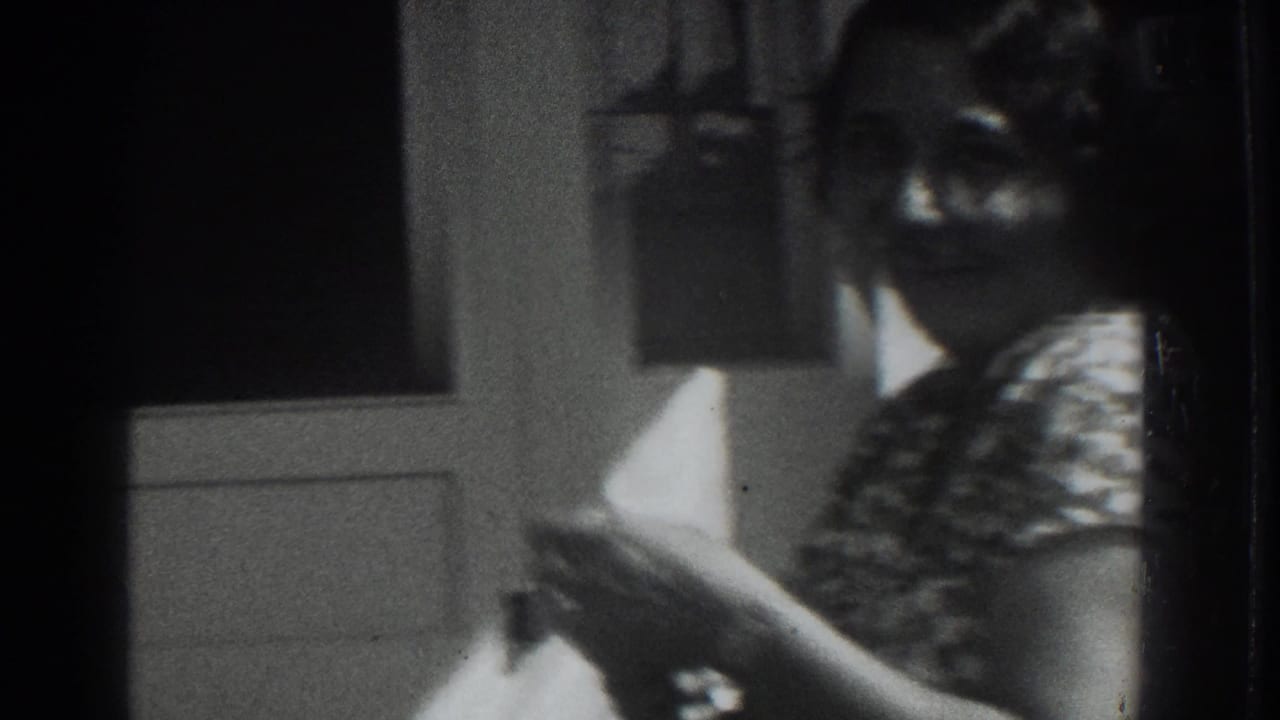 1937 Vacaville home-movie frame showing a seated woman indoors, partly blocked by a second figure and dark film edges.