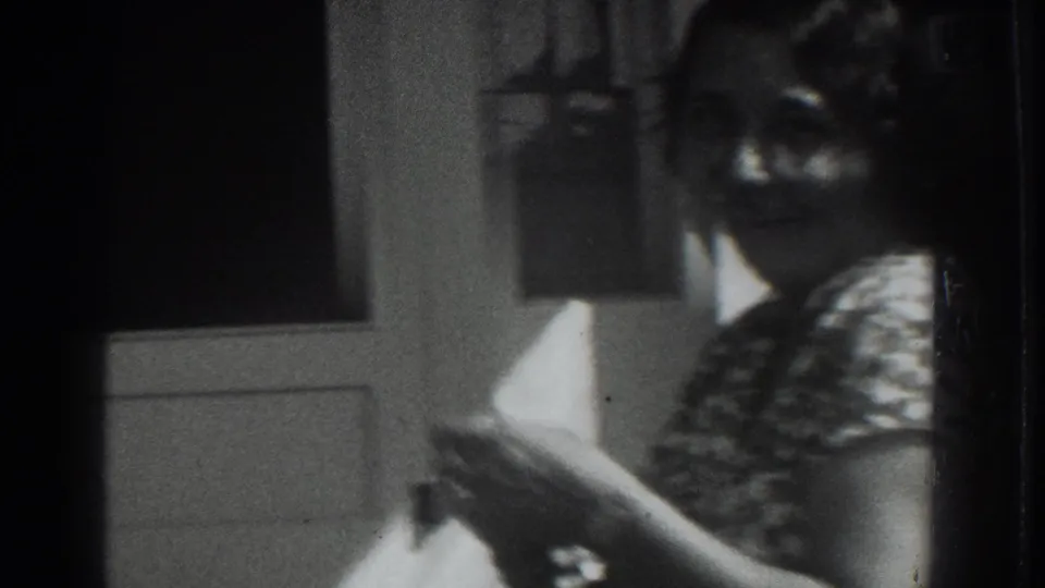 1937 Vacaville home-movie frame showing a seated woman indoors, partly blocked by a second figure and dark film edges.