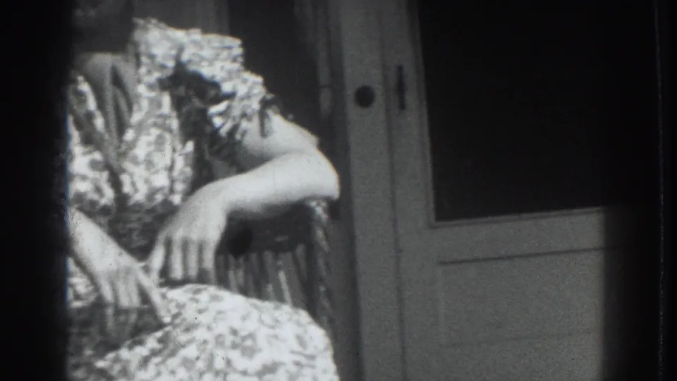 1937 Vacaville frame of a woman in a patterned dress seated near interior doors, with high contrast and soft focus.