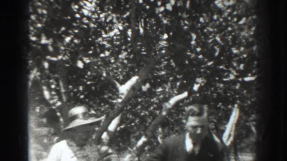 In 1937 Vacaville, a woman in a white dress and wide-brimmed hat stands beneath orchard trees with a suited man partly visible.