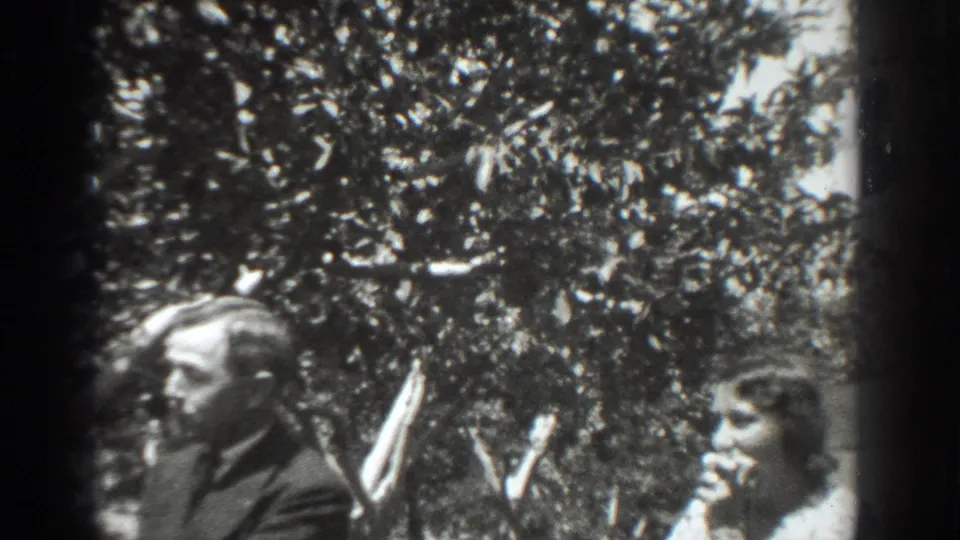 The orchard home-movie frame shows a suited man in profile and a young woman nearby, both partly cropped by the 8mm contact sheet.