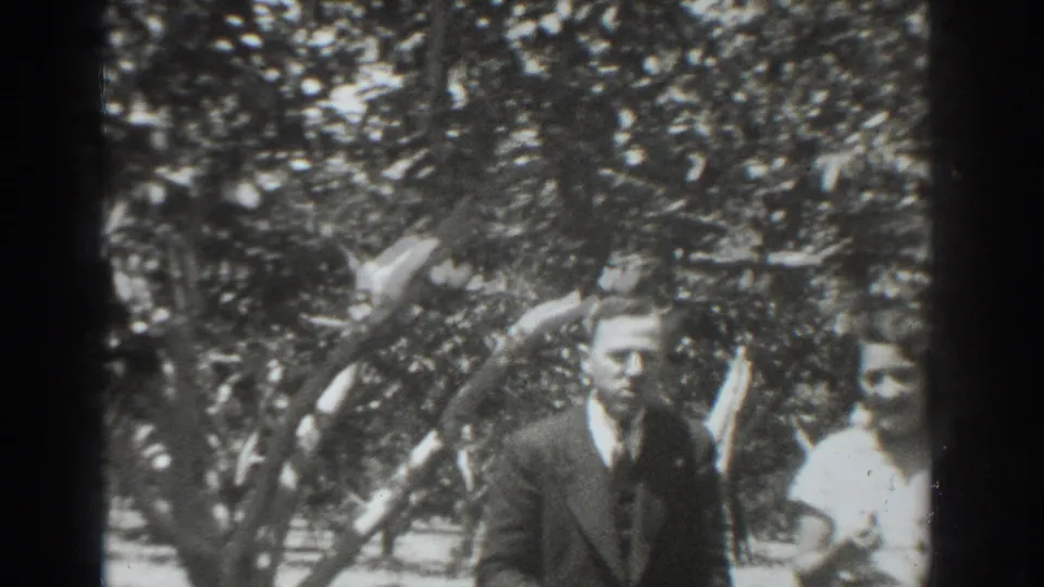 The man in a dark suit and the woman in a light dress are more visible under the tree in the 1937 Vacaville footage.