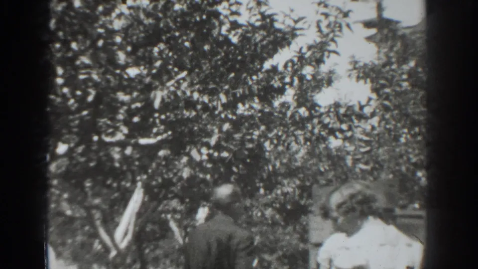 1937 Vacaville garden view with a dark-suited man and light-dressed woman under heavy foliage.