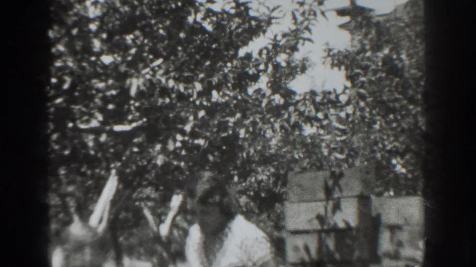 In metadata-supported 1937 Vacaville footage, two adults stand in a shaded garden as the man faces the woman.