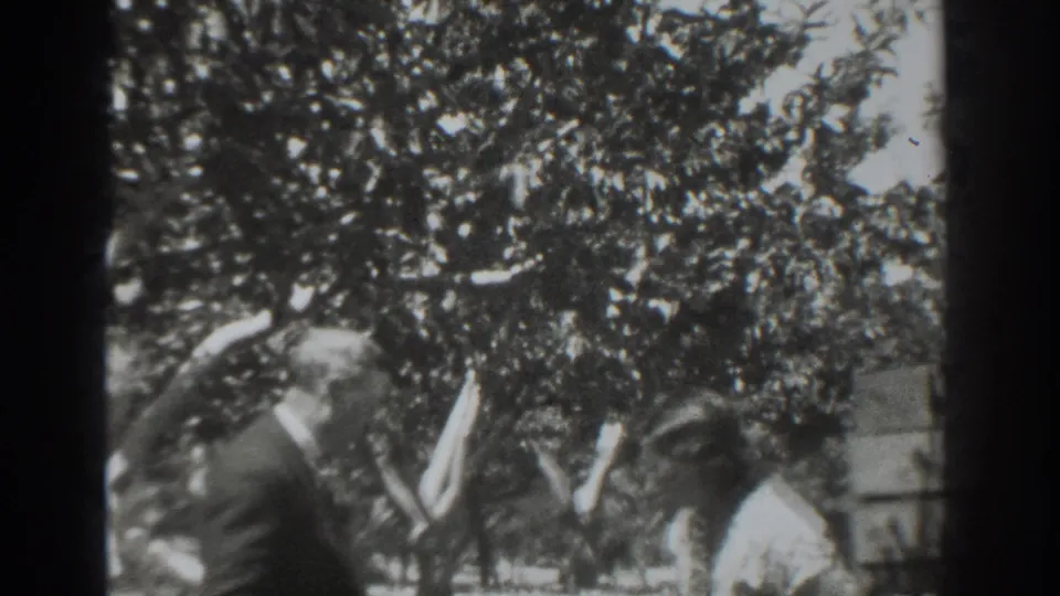 Two adults continue their outdoor exchange, framed by trees and a low garden structure in the 1937 Vacaville home movie.