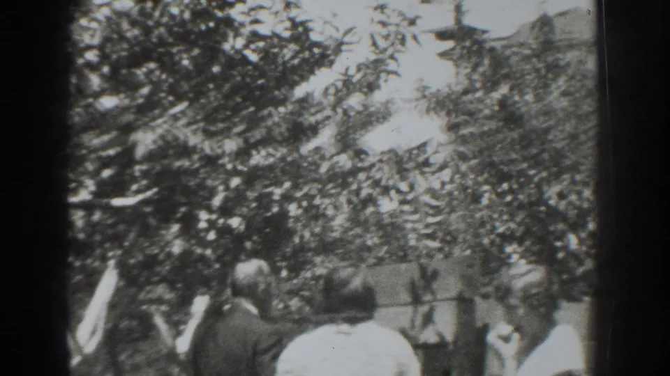 In 1937 Vacaville home-movie footage, adults gather beneath leafy orchard trees near a wall or fence.