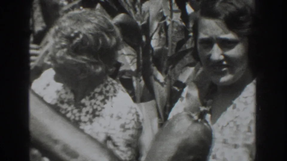 1937 Vacaville frame showing two women in patterned dresses beside leafy branches, with one facing the camera.