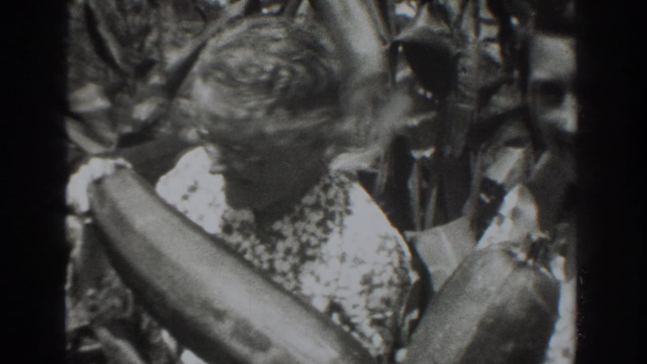 Older woman holding a large vegetable among tall garden plants.