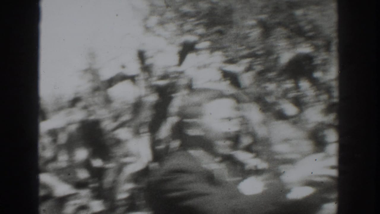 Blurred adults moving through a leafy crop field in black-and-white home-movie footage.