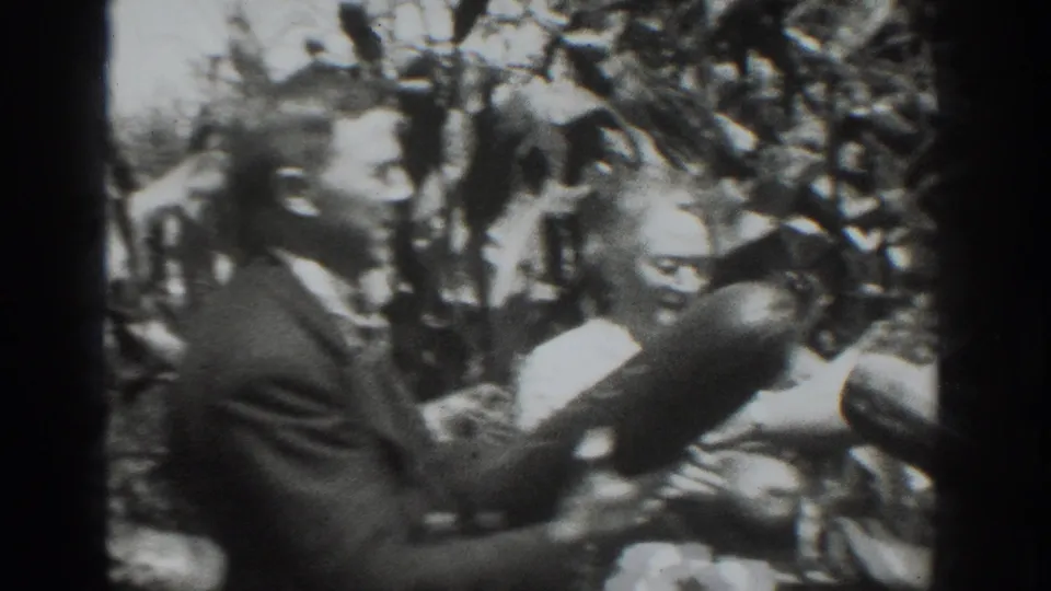 1937 Vacaville footage shows adults in period clothing comparing elongated harvested vegetables in a crowded field setting.