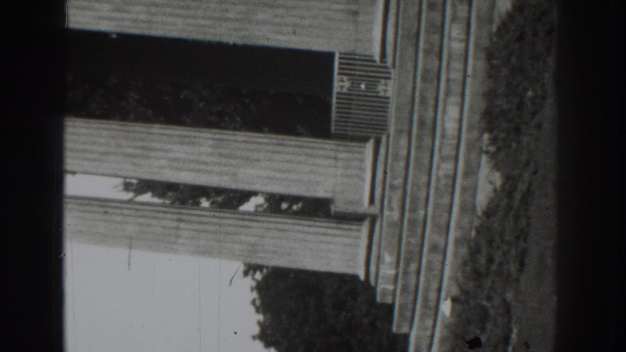 Partial upside-down porch view with window awning, wall, trees, and film gate edges.