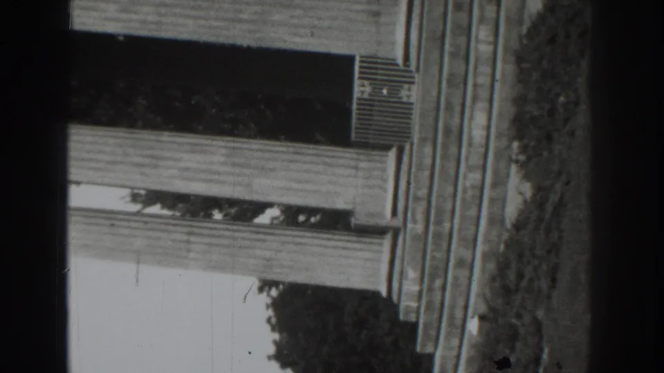 Upside-down 8mm frame from the Vacaville 1937 clip showing a porch exterior, awning, wall, trees, and dark film edges.