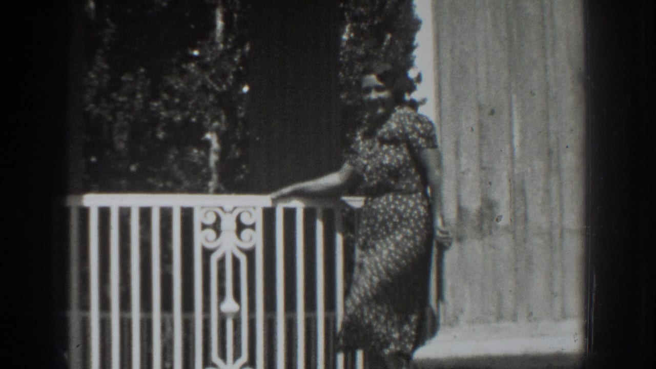 Woman in a patterned dress stands by a white balcony railing and column.