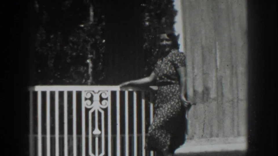 The woman remains posed on the balcony in Vacaville, California, with a decorative rail and column framing the shot.