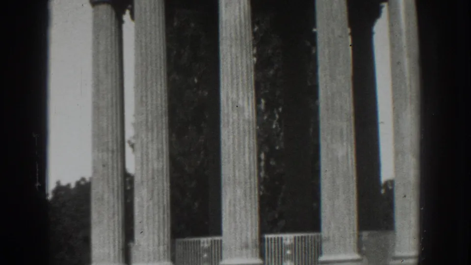 1937 Vacaville frame with tall classical columns, dark foliage, railings, and soft black-and-white 8mm exposure.