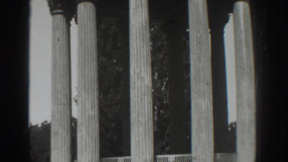 Black-and-white 1937 Vacaville home-movie still showing several fluted columns, a railing, trees, and film grain.