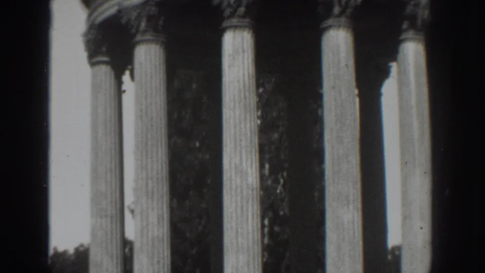 1937 Vacaville home-movie frame showing Roman-style columns, ornate capitals, bright sky, and dark background foliage.