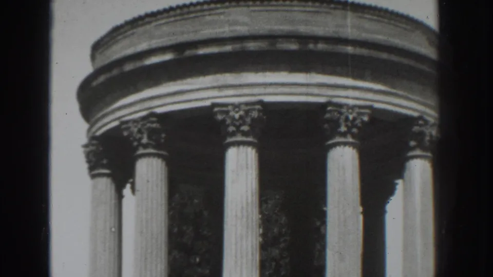 1937 Vacaville frame showing more of the circular building's columns, with dark tree shapes visible through the open structure.