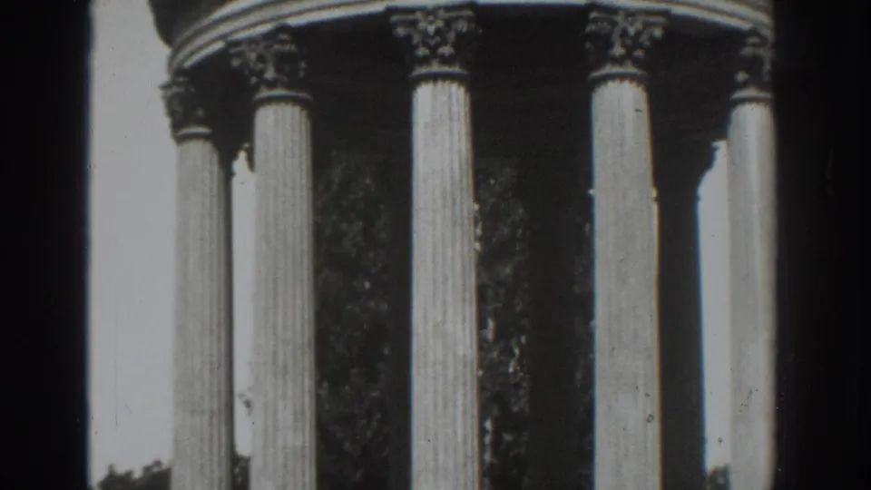 1937 Vacaville home-movie frame showing a close view of classical fluted columns with leafy trees behind them.