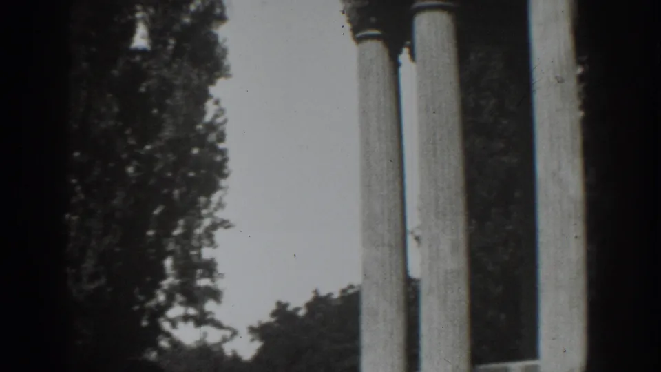 Close handheld 1937 Vacaville view of column shafts, foliage, and pale sky in black-and-white 8mm footage.