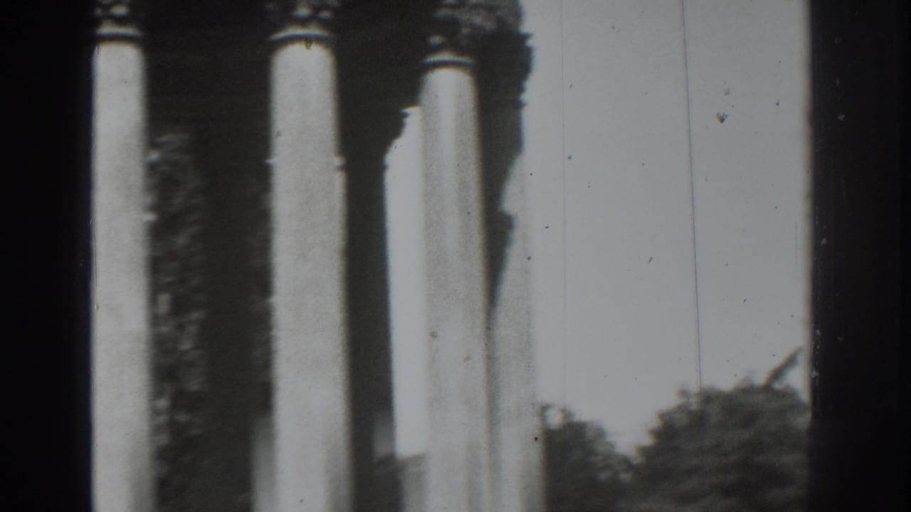 Tall Roman-style columns beside dark film-frame edges with trees and sky beyond.
