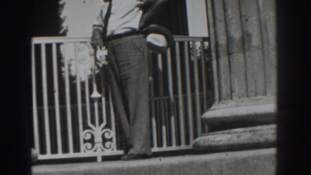 Man in trousers stands near an ornate railing and large fluted column.