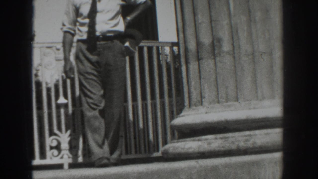 The man passes close to the camera in the Vacaville 1937 exterior scene, with the railing and column base behind him.