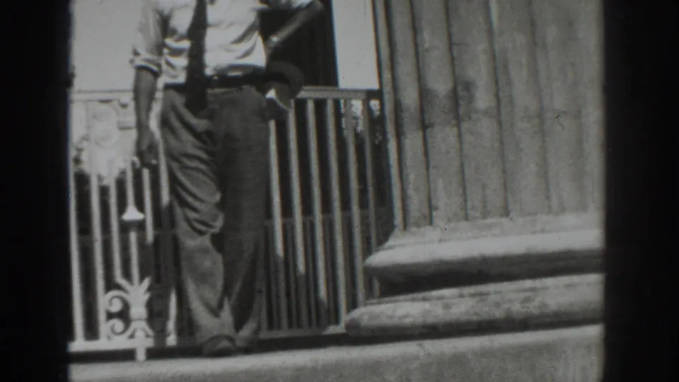 The man passes close to the camera in the Vacaville 1937 exterior scene, with the railing and column base behind him.
