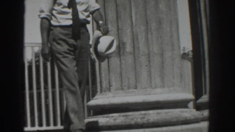 In 1937 Vacaville footage, a formally dressed man descends stone steps beside tall columns while carrying a light-colored hat.