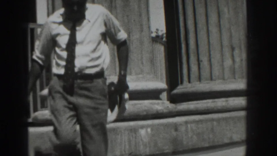 A closer frame shows the man's shirt, tie, trousers, and hat as he descends the exterior steps in Vacaville.