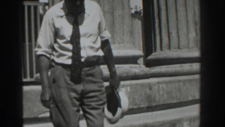 Near the end of the 1937 Vacaville clip, the man passes close to camera with his hat held low against the columned exterior.