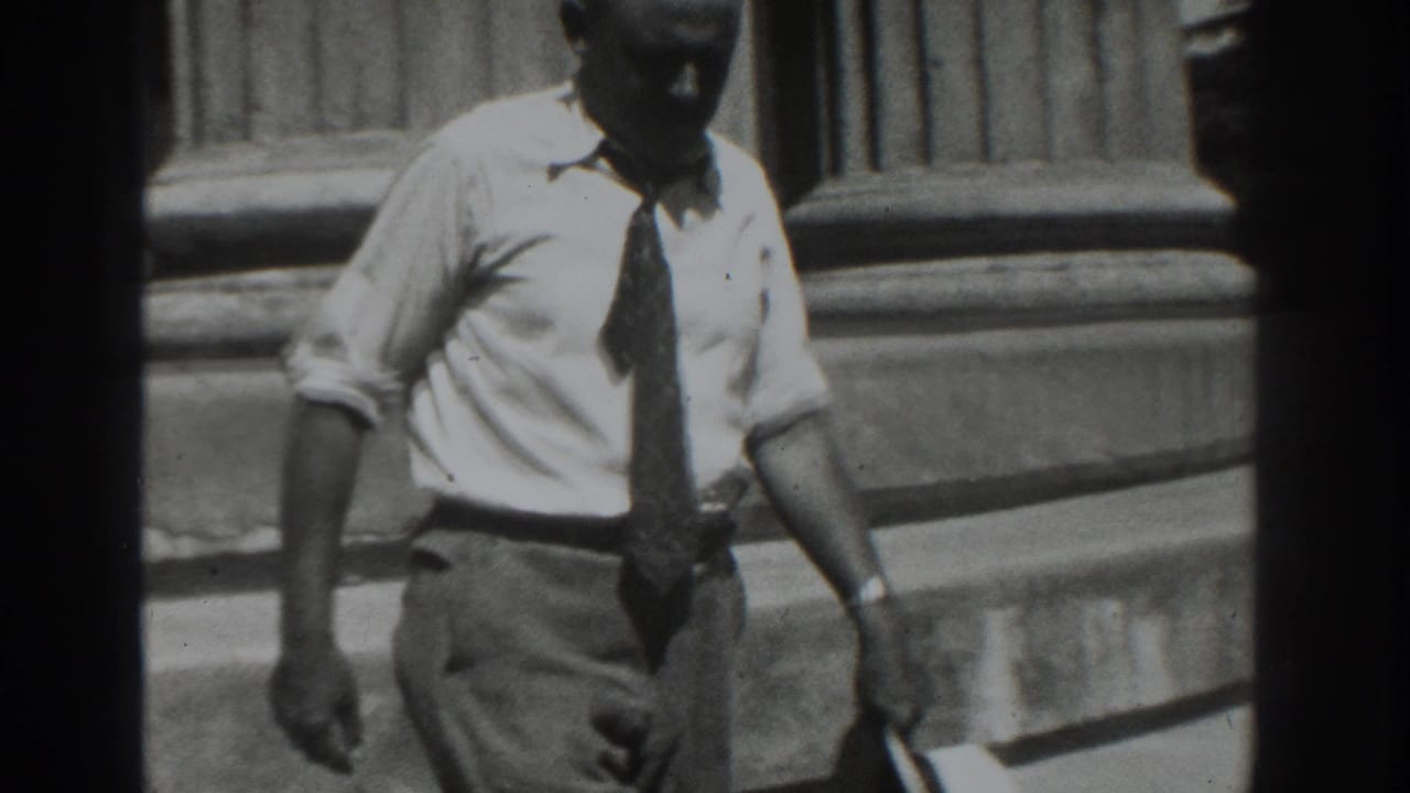 Adult man in a white shirt and tie stands or walks near stone steps.