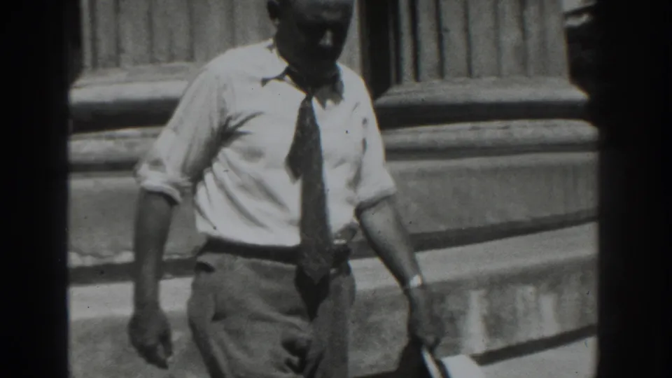 In 1937 Vacaville footage, an adult man in a white shirt and tie is seen near stone steps outside a building.