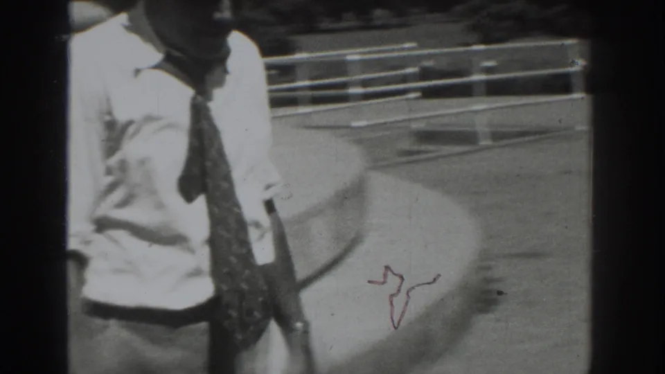 A 1937 Vacaville frame shows the man in a white shirt and tie moving past a column with steps and pavement behind him.