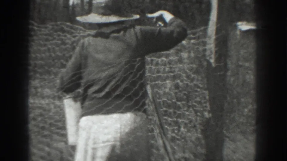 Side view of the woman at the chicken wire fence, her hat shading her face as she works near the post in 1937 Vacaville.