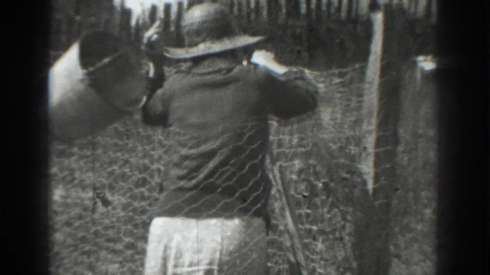 In 1937 Vacaville home-movie footage, a woman in a wide-brimmed hat works near chicken wire fencing and rough wooden posts.
