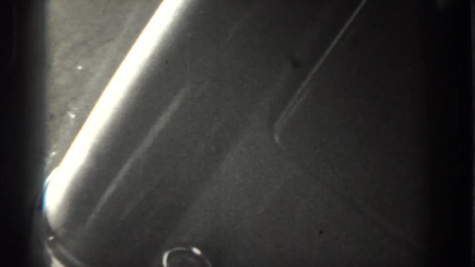 1937 Vacaville 8mm frame showing a strong diagonal light leak, dark exposure, grain, and a small bright curved mark near the bottom.