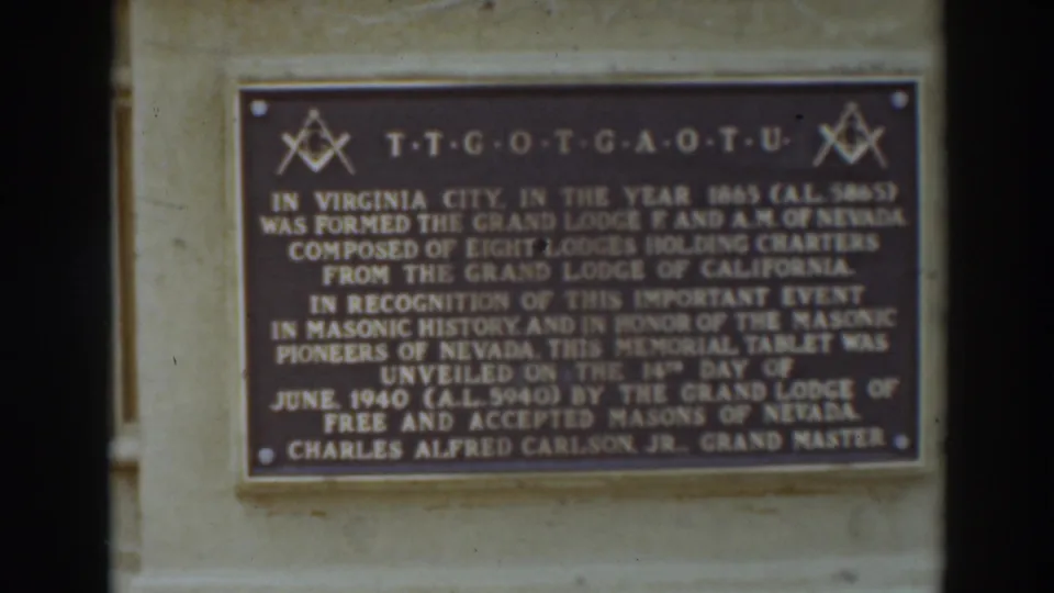 Soft-focus 8mm view of the bronze Masonic plaque, showing raised lettering, symbols, and the wall-mounted setting.
