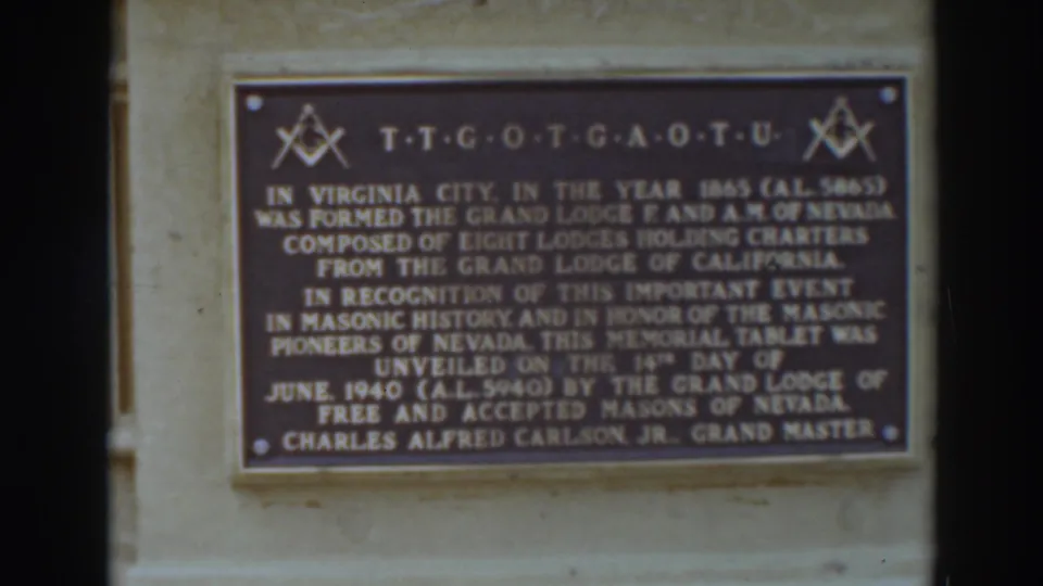 Close 8mm frame of a Masonic memorial tablet on a stone wall in Virginia City, with gold lettering and square-and-compass symbols.