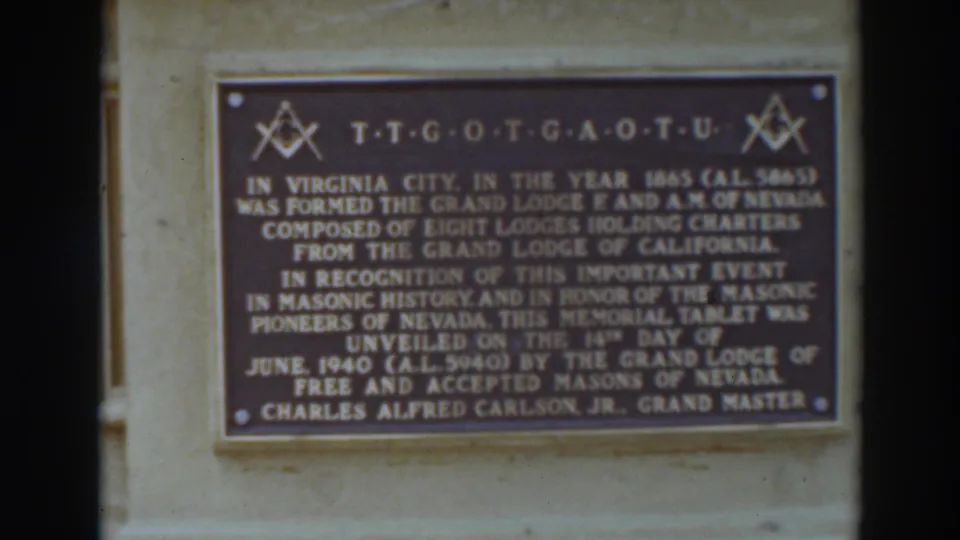 Final close frame of the Virginia City Masonic memorial plaque, with the bronze tablet, gold text, and stone wall still visible.