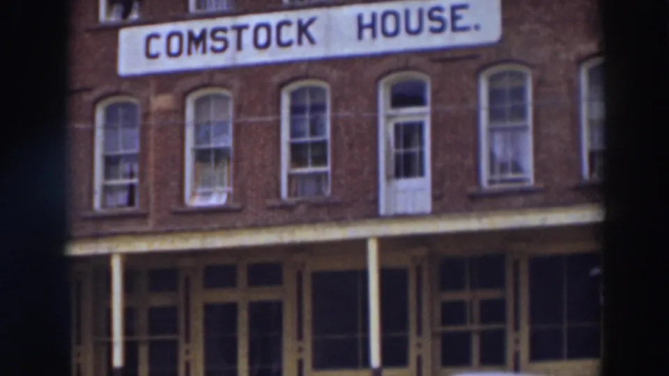 1937 8mm view of the Comstock House sign on a brick facade in Virginia City, California, framed by upper windows and porch details.