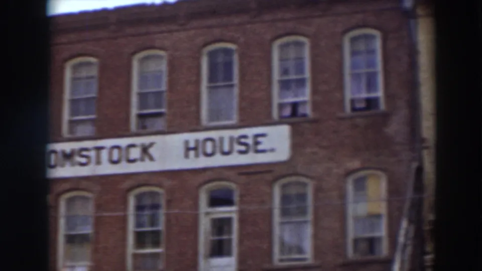 A shifted 8mm frame shows part of the Comstock House sign on the brick facade, with arched windows and soft handheld framing.