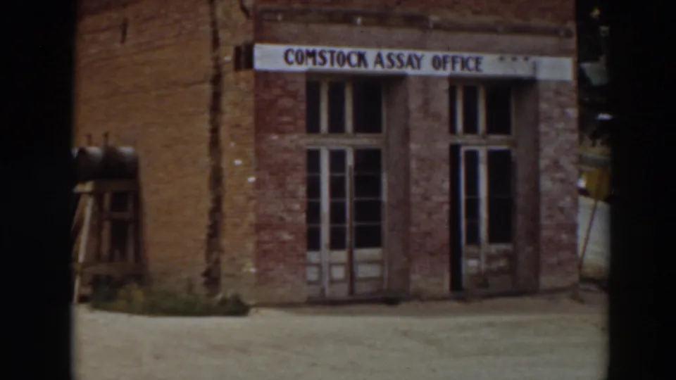 1937 8mm view of the Comstock Assay Office in Virginia City, California, showing a brick frontage, sign, and double doors.