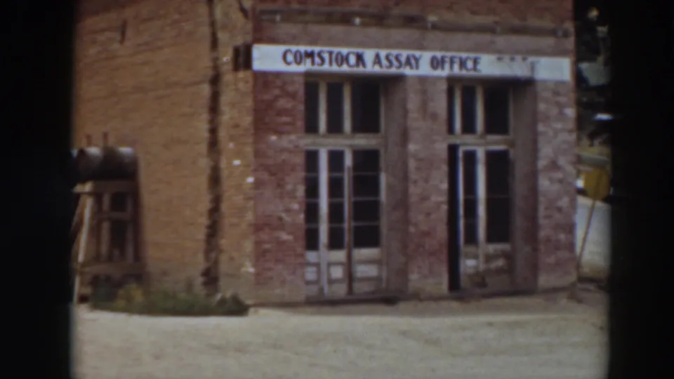 Closer 1937 8mm view of the Comstock Assay Office facade, with weathered brick, tall doors, and the sign across the top.