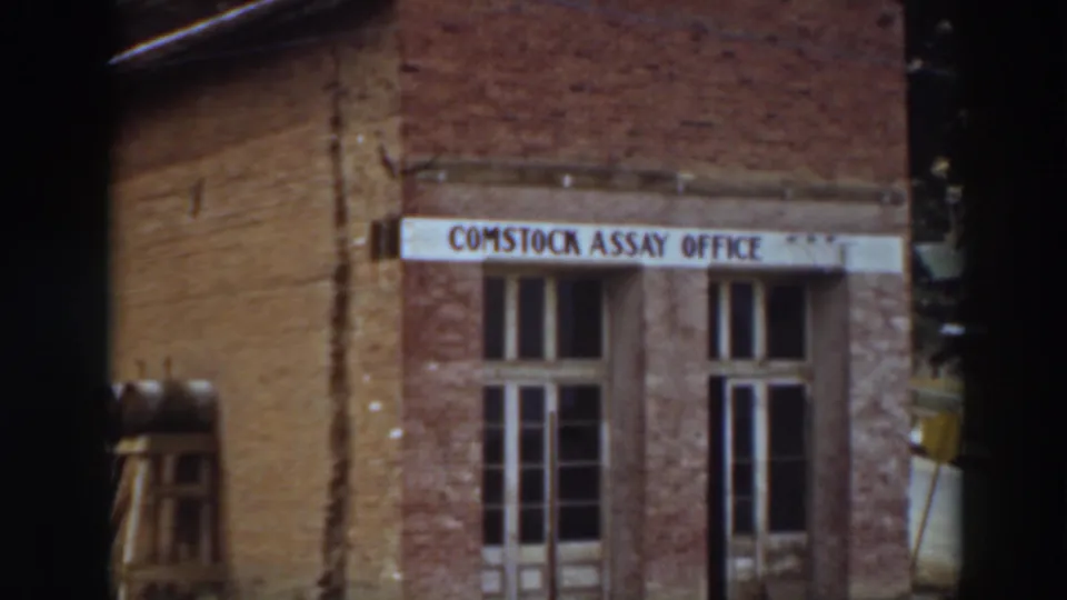 The upward pan centers the readable Comstock Assay Office sign and upper doorway area of the brick building in Virginia City.