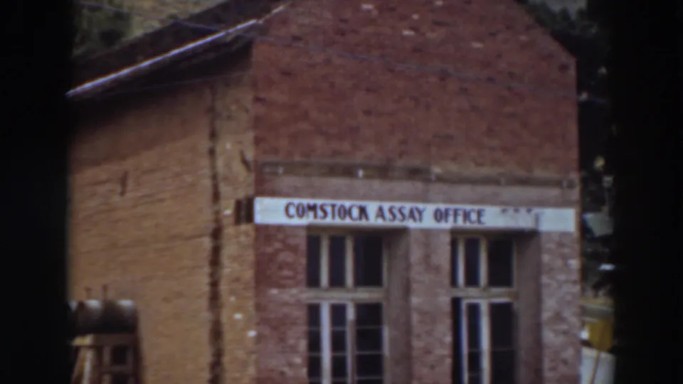 The 8mm frame shows the Comstock Assay Office sign, weathered brickwork, and tall windows during the upward pan.