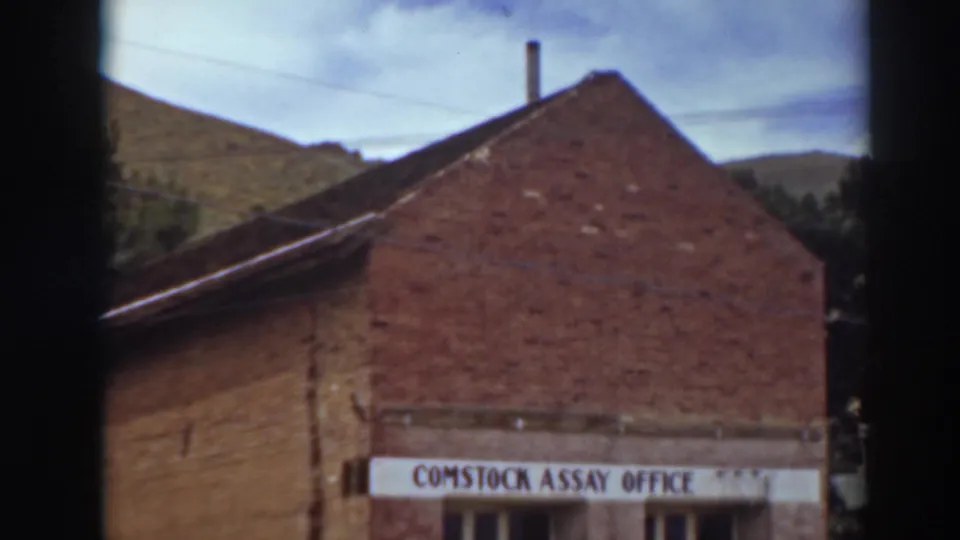 Signed Comstock Assay Office brick building in Virginia City, California, framed close with gabled roof, chimney, sky, and hillside visible.