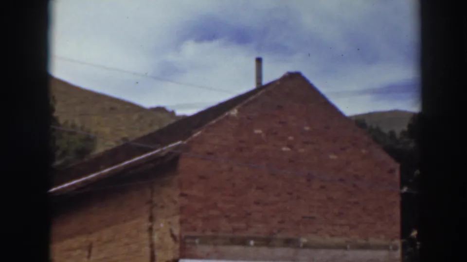 The camera holds on the Comstock Assay Office, emphasizing its brick gable end, roofline, partial sign, window openings, and rolling hillside.